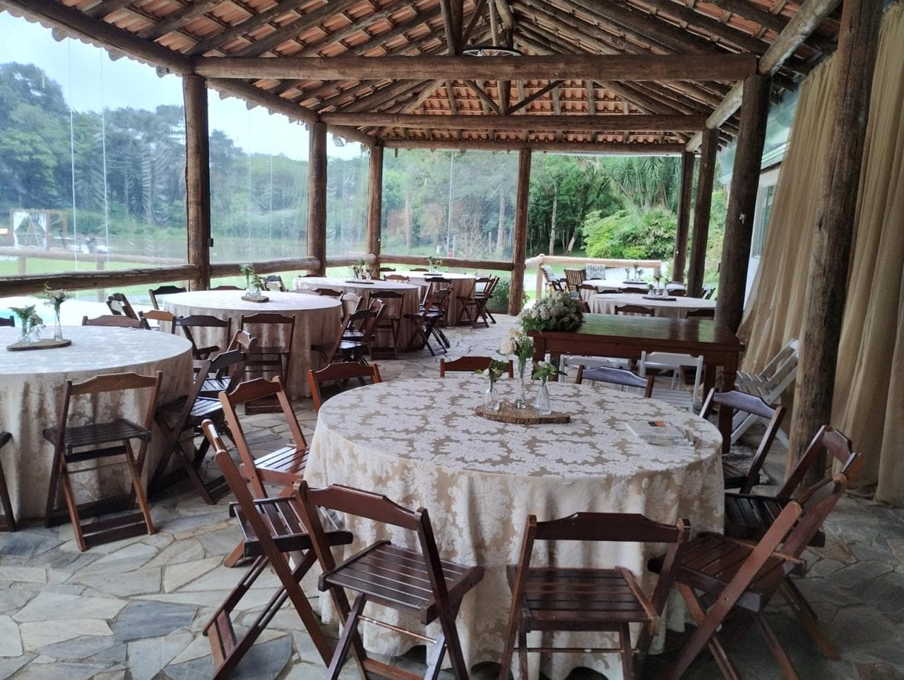 Salão rústico com mesas decoradas e vista para a natureza